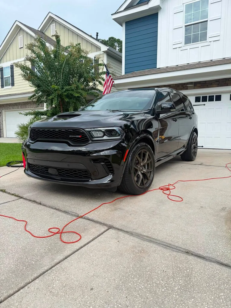 Black Dodge SUV with reflections across its hood and doors on a residential driveway