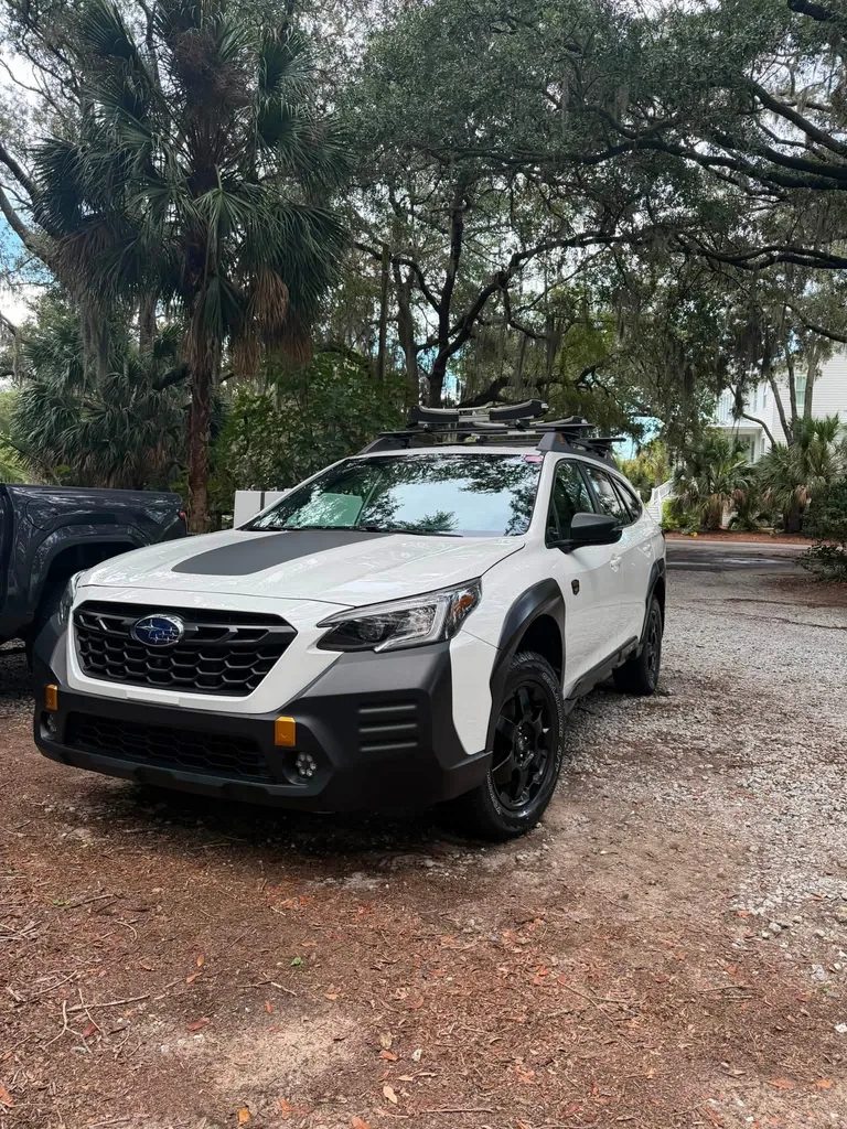 White Subaru SUV with a roof rack beneath trees